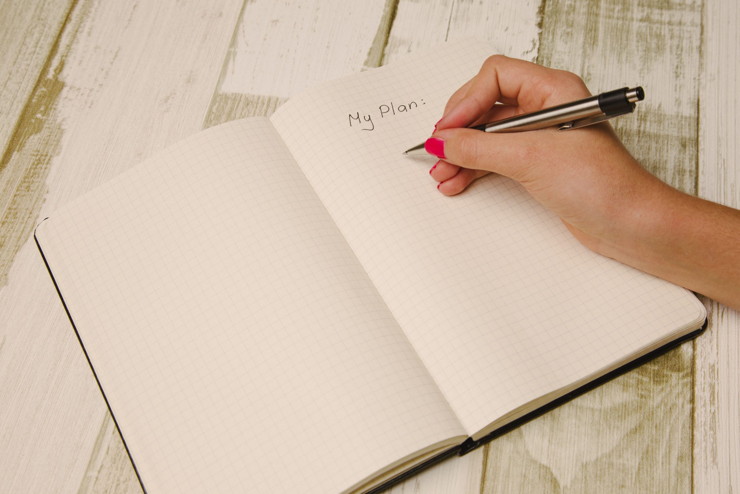 Female hand holding a pen and writing a plan in a planner for planning a digital job ad.